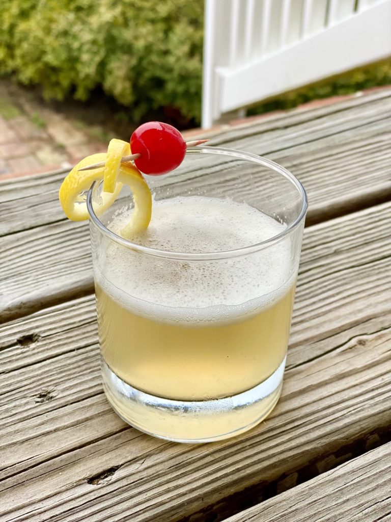 bay sour cocktail with lemon peel and cherry on deck
