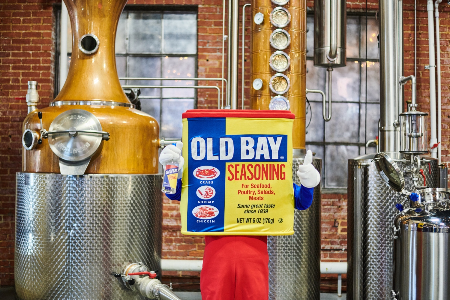 old bay mascot holding old bay vodka bottle in distillery