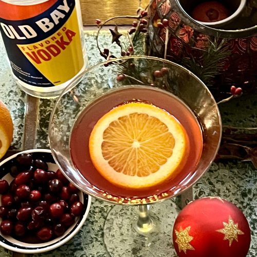 martini glass with orange slice cranberries and old bay vodka bottle