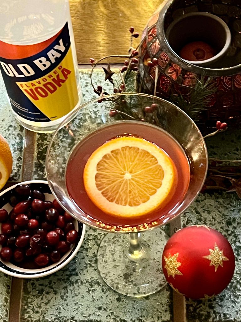 martini glass with orange slice cranberries and old bay vodka bottle