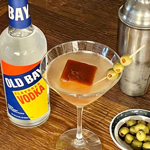 martini glass with olives and old bay vodka bottle