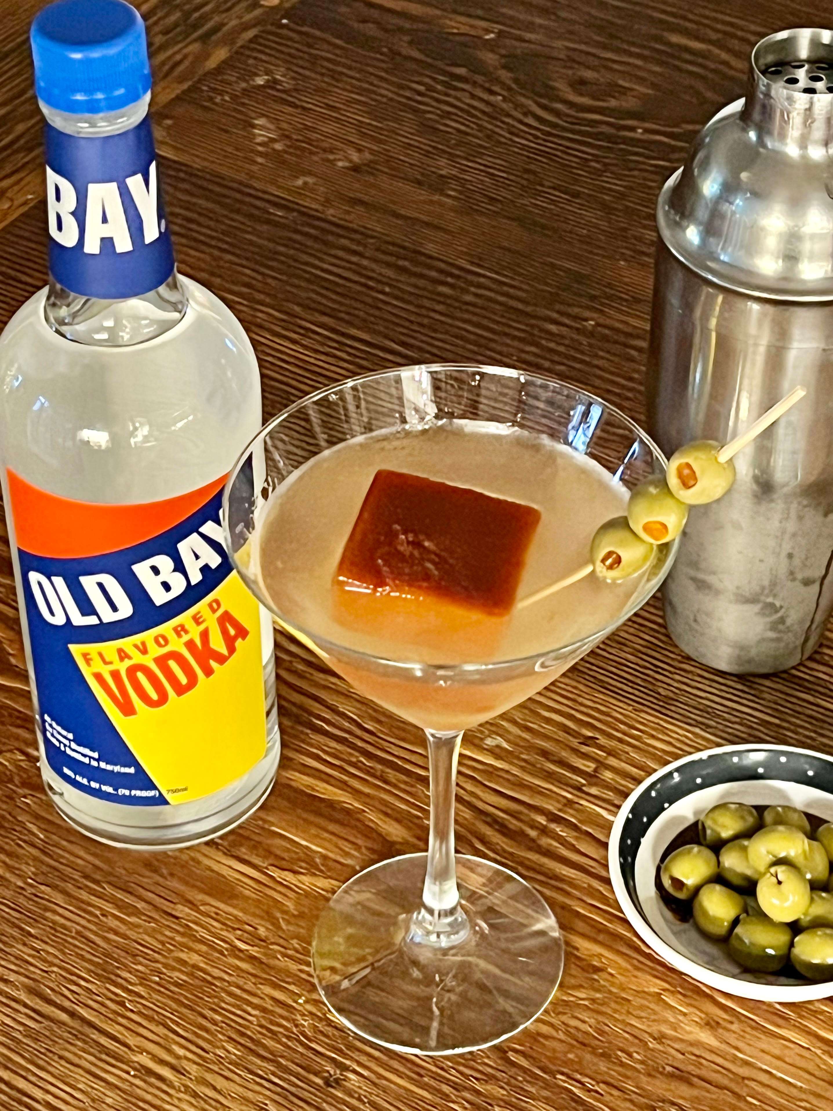 martini glass with olives and old bay vodka bottle