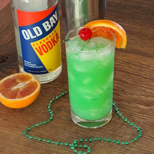 green cocktail with cherry orange slice old bay vodka and green beads