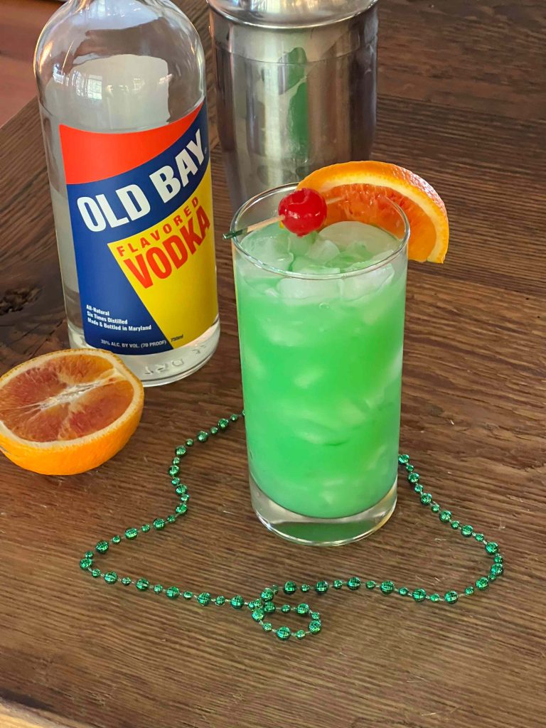 green cocktail with cherry orange slice old bay vodka and green beads