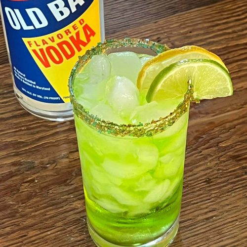 green cocktail with lemon lime slices and old bay vodka bottle