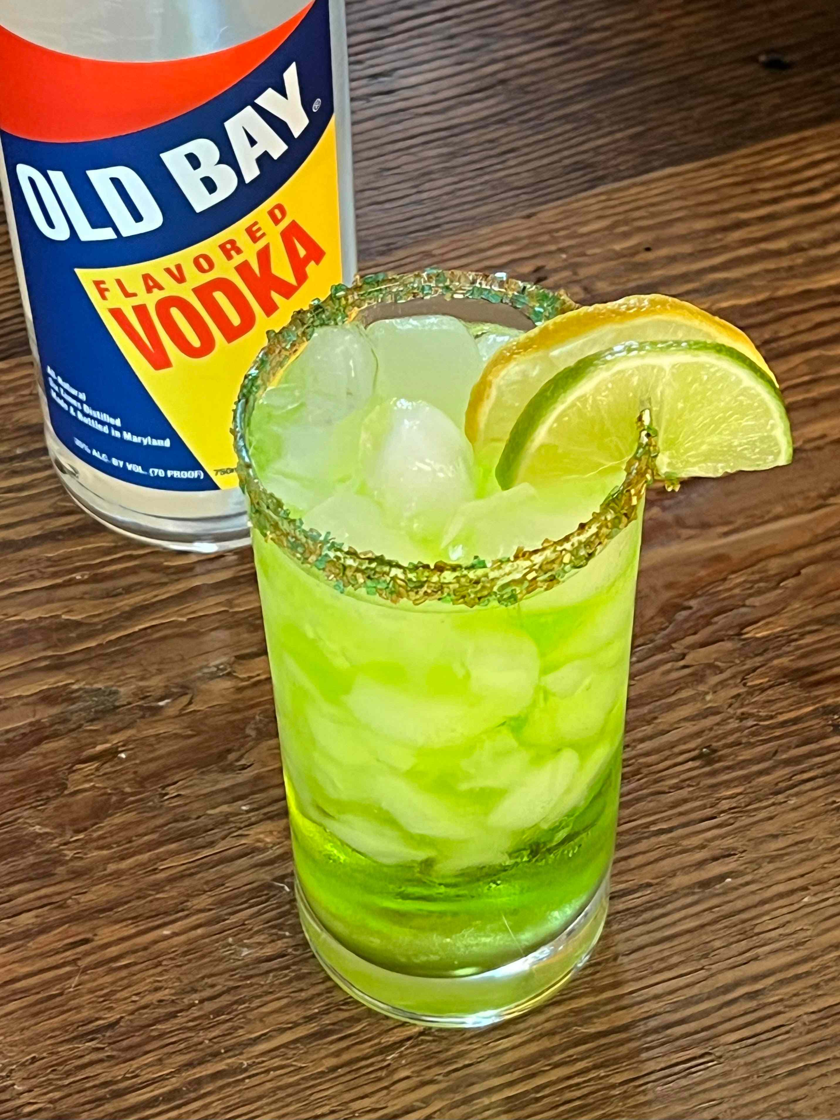 green cocktail with lemon lime slices and old bay vodka bottle