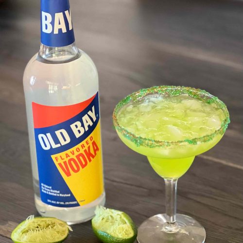 green cocktail with old bay vodka bottle and limes