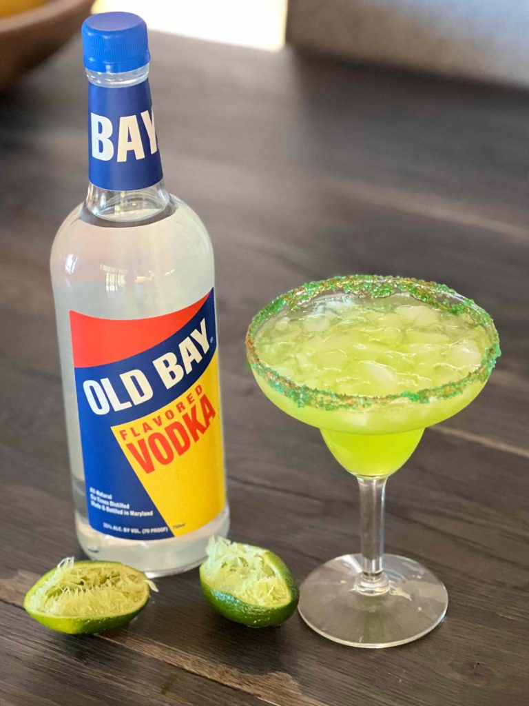 green cocktail with old bay vodka bottle and limes